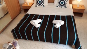 Una cama bien hecha con un edredón a rayas, dos almohadas con diseños circulares y dos toallas enrolladas en el suelo.