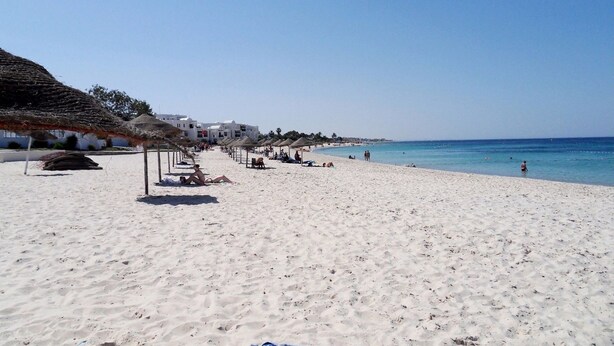 Una playa de arena blanca, sombrillas de paja y edificios blancos a lo largo de la costa.