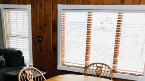 Un comedor con una mesa y sillas de madera, una ventana con persianas y vistas al exterior.