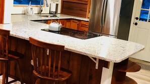 Una cocina con una isla central, taburetes de madera, electrodomésticos de acero inoxidable y una ventana con vistas.