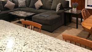 Una sala de estar moderna con un sofá modular, una mesa de comedor y una cocina con encimeras de granito.