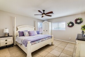 A bedroom with a four-poster bed, a nightstand with a lamp, a dresser, and a ceiling fan.