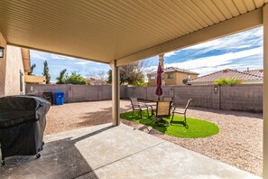 A covered patio area with a barbecue grill, outdoor furniture, and a small lawn.