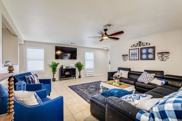 A living room with a black leather sofa, blue armchairs, a coffee table, and a TV mounted on the wall.
