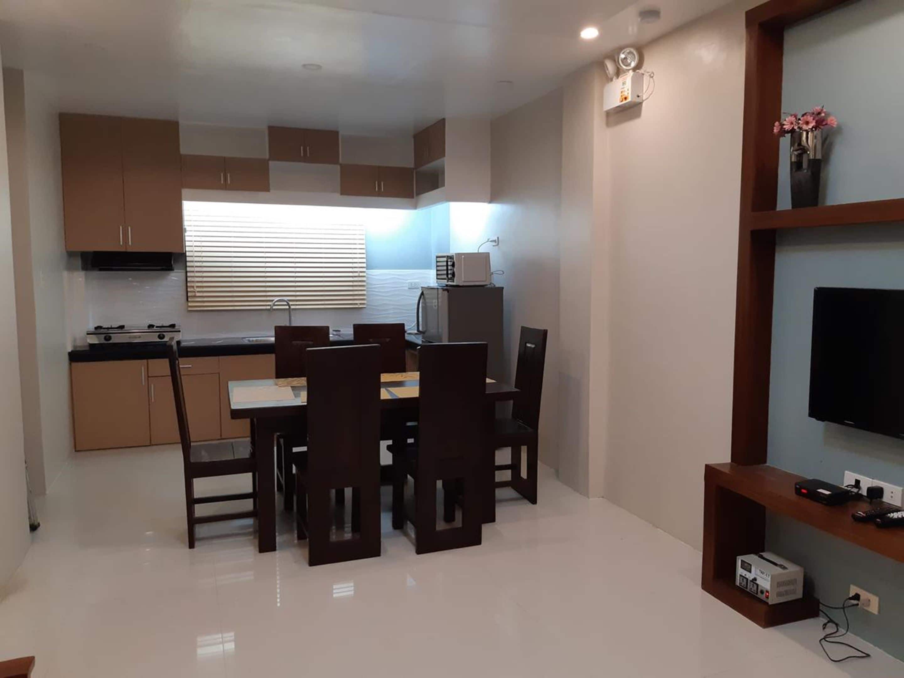 A compact kitchen with a stove, microwave, and sink. There is a dining area with a table and chairs. A flat-screen TV is mounted on the wall.