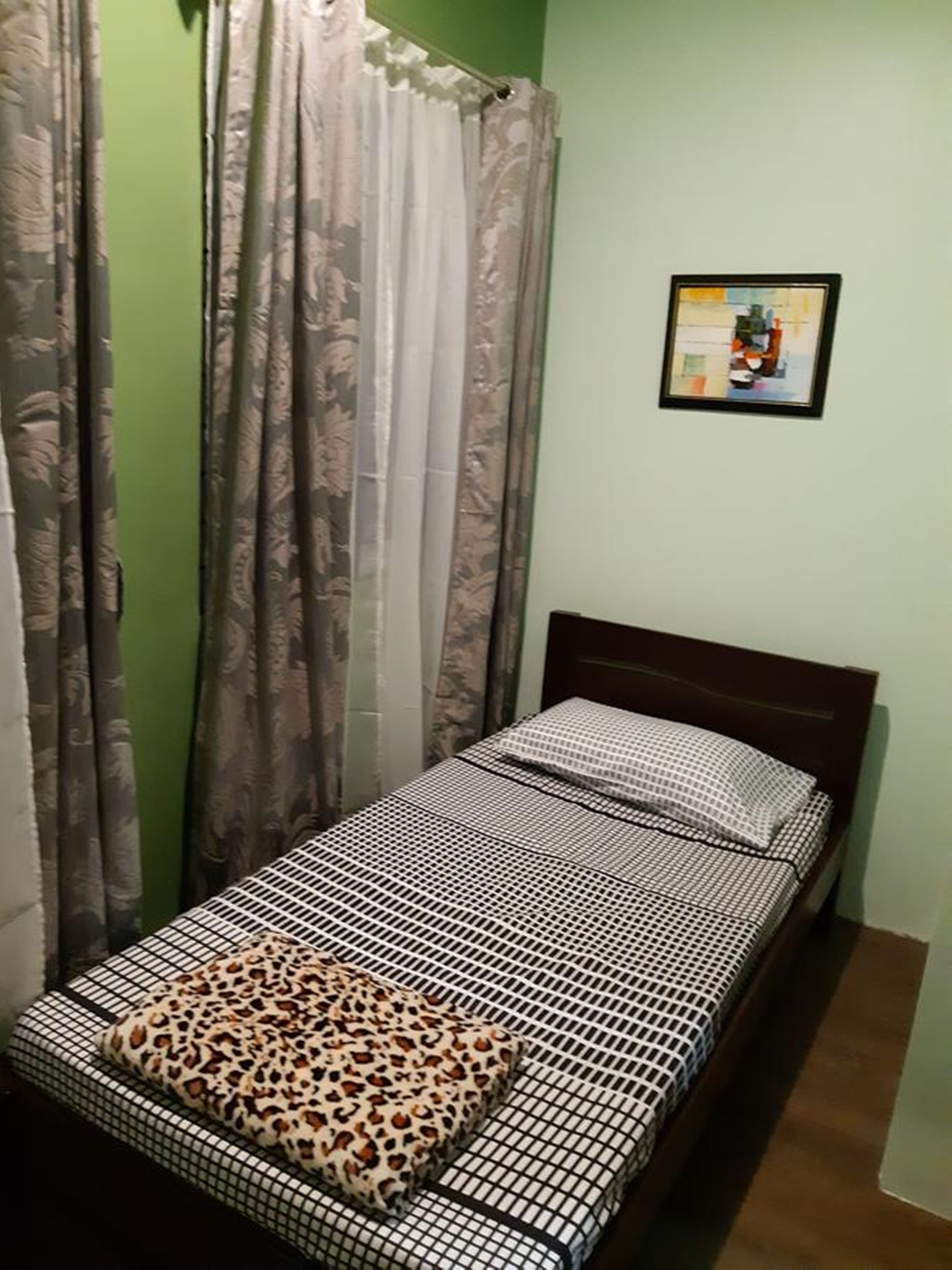 Une petite chambre avec un lit simple, une couvre-lit à motifs, un coussin à imprimé léopard et un tableau encadré accroché au mur.