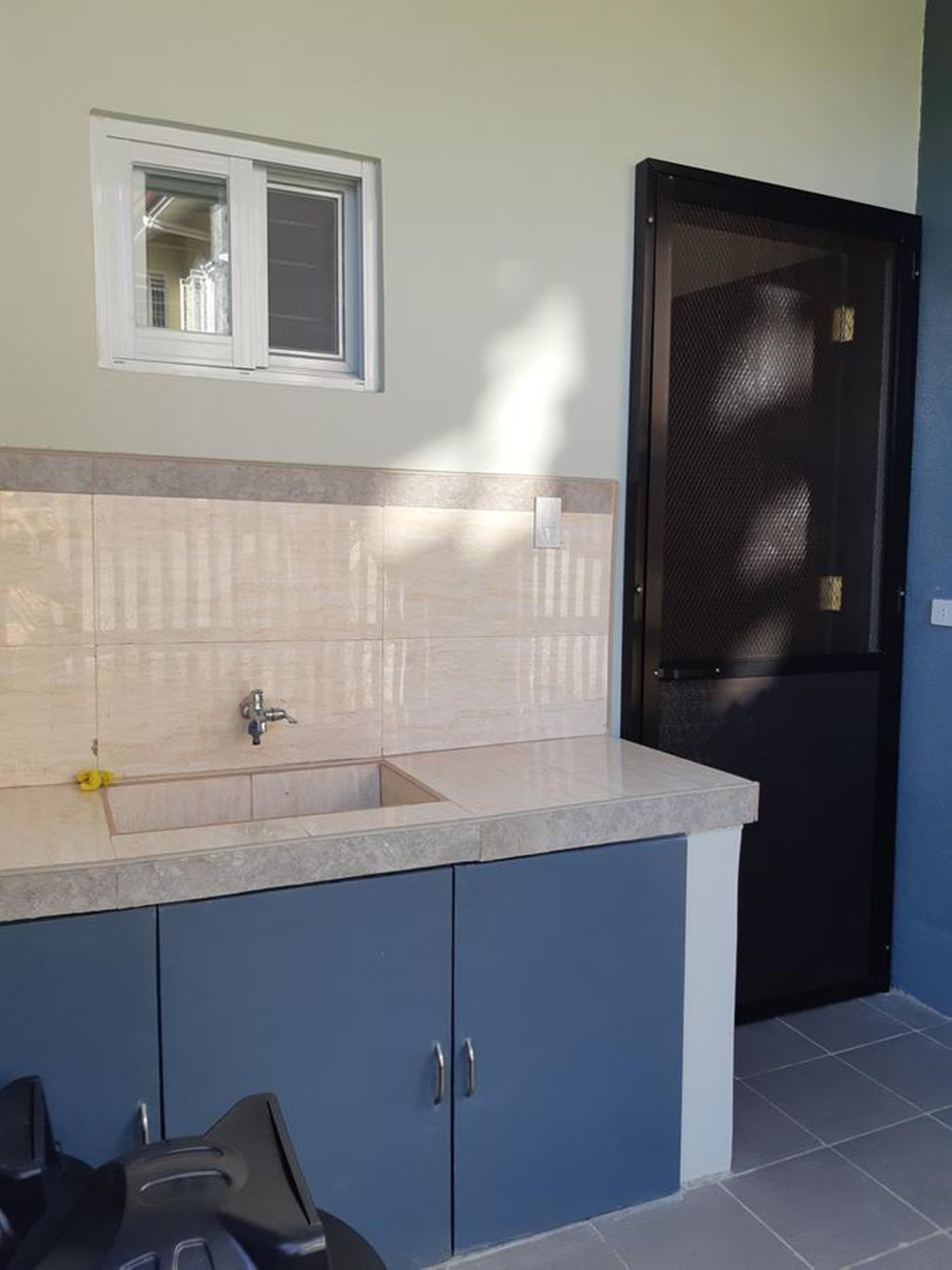 A kitchen with a sink, cabinets, a window, and a door.