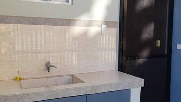A kitchen with a sink, cabinets, a window, and a door.