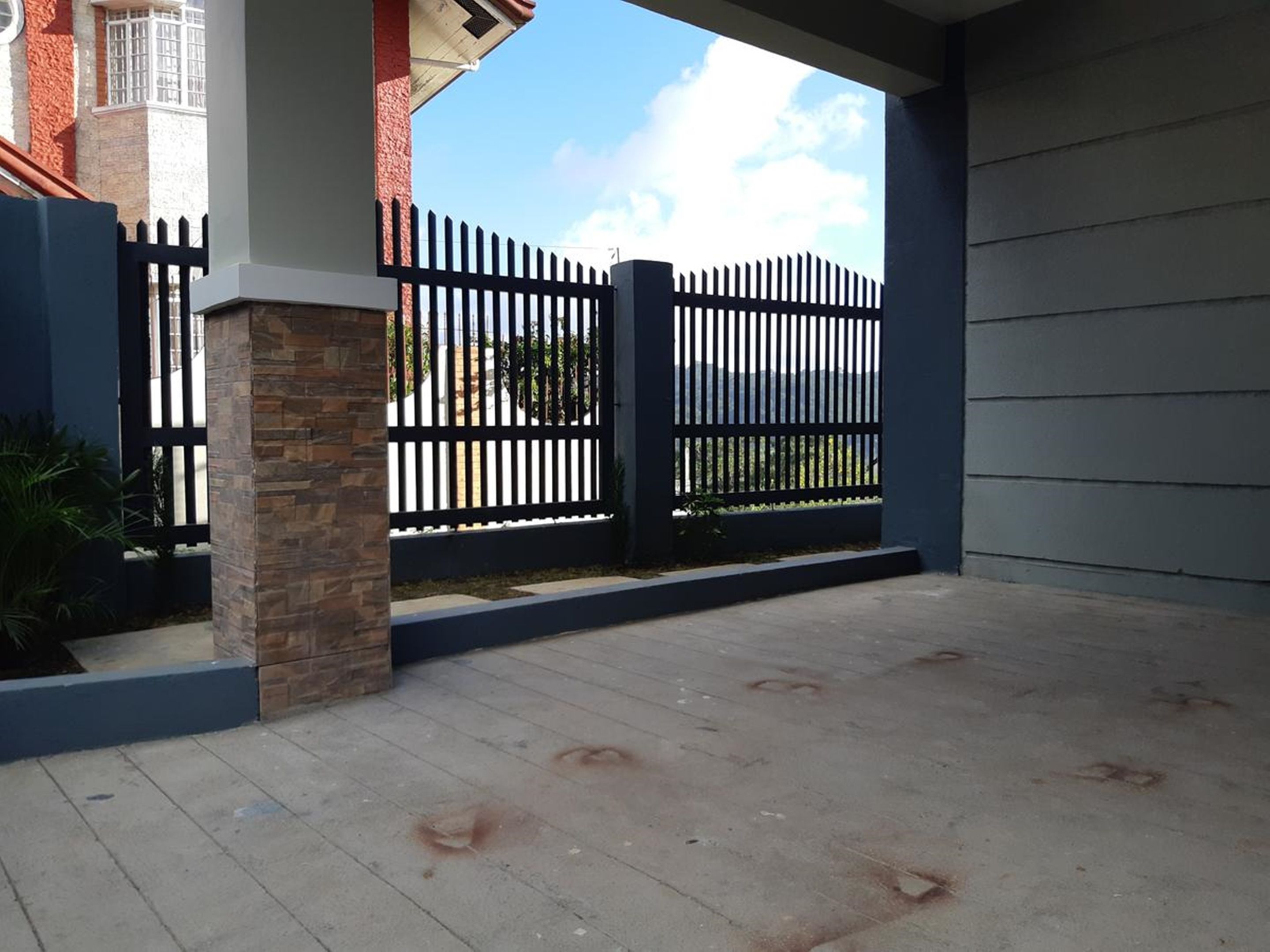 A covered outdoor area with a concrete floor, a black metal fence, and a stone pillar.