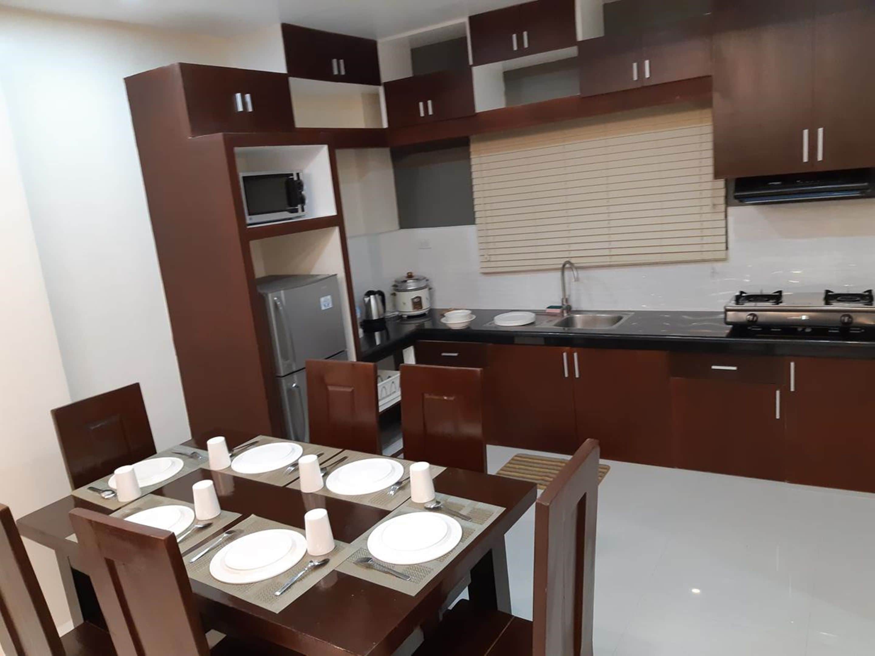 A modern kitchen with dark brown cabinets, a black countertop, and a dining table set for four.