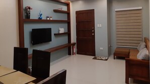 A modern living room with a flat-screen TV, wooden shelving, a sliding door, and a window with blinds. - Restful 3BR Hillside Duplex (Baguio)
