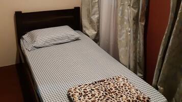 A small, neatly made bed with a patterned bedspread and a leopard print pillow. There is a framed picture on the wall above the bed.