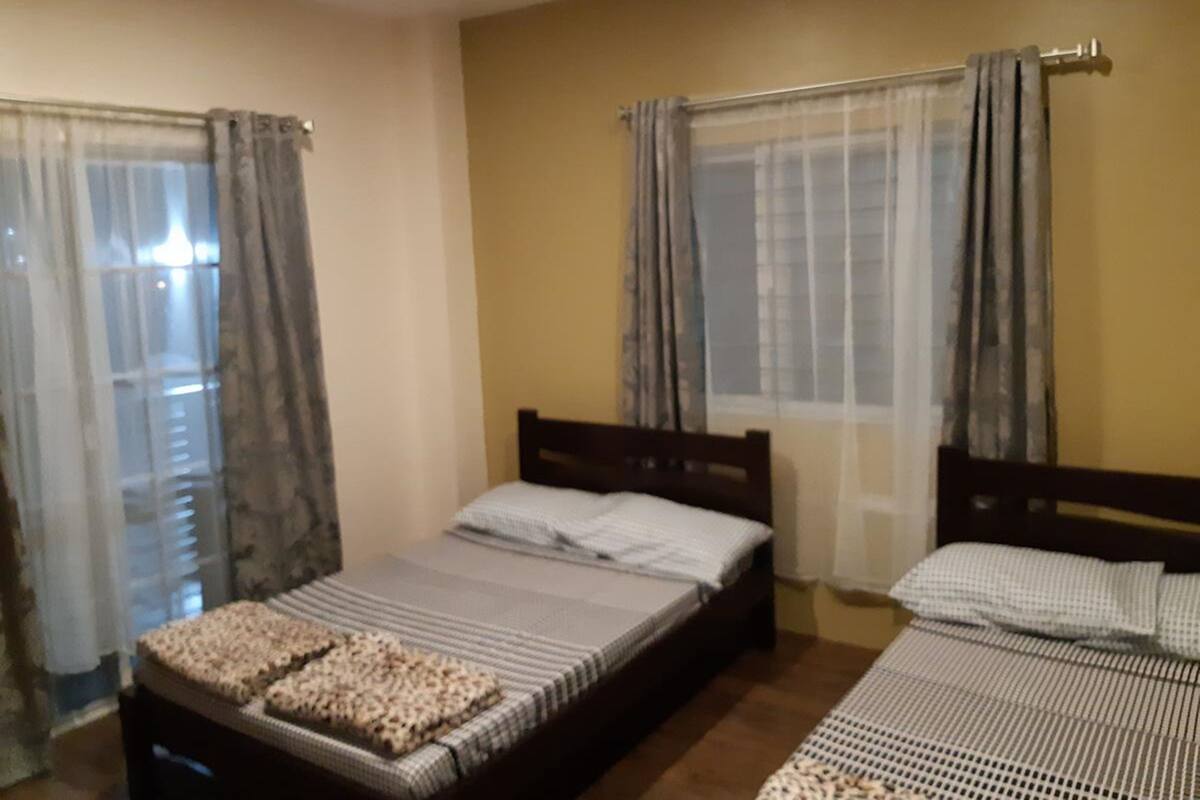 A room with two single beds, a wooden headboard, and a window with curtains.