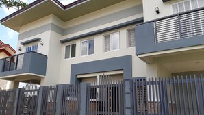 A modern two-story residential building with a grey and white facade, a balcony on the upper floor, and a gated entrance. - Restful 3BR Hillside Duplex (Baguio)