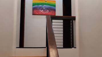 Una escalera con peldaños de madera y barandilla metálica, que conduce a una plataforma con un cuadro de colores y dos unidades de aire acondicionado en la pared.
