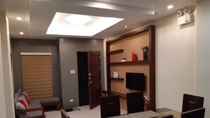 A modern living room with a dining area, a built-in TV, and a ceiling light fixture. - Restful 3BR Hillside Duplex (Baguio)
