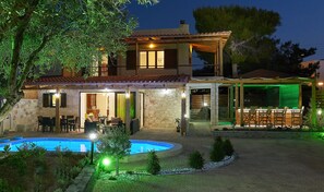 Una casa de dos pisos con piscina, mobiliario exterior y un patio cubierto.