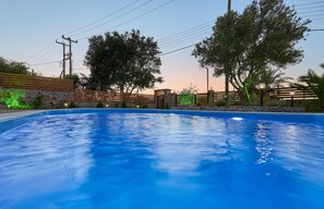 Una piscina con muro de piedra y cerca de madera, rodeada de árboles y líneas eléctricas.