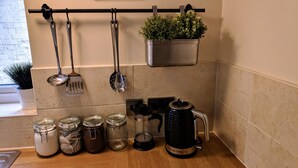 Una encimera de cocina con utensilios de acero inoxidable, tarros de vidrio, una cafetera y una planta colgante.