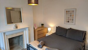 Un dormitorio con cama, mesita de noche, cómoda, espejo y chimenea.