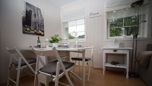A dining area with a white table, four chairs, a small side table with a candle, and a window with a view of trees.