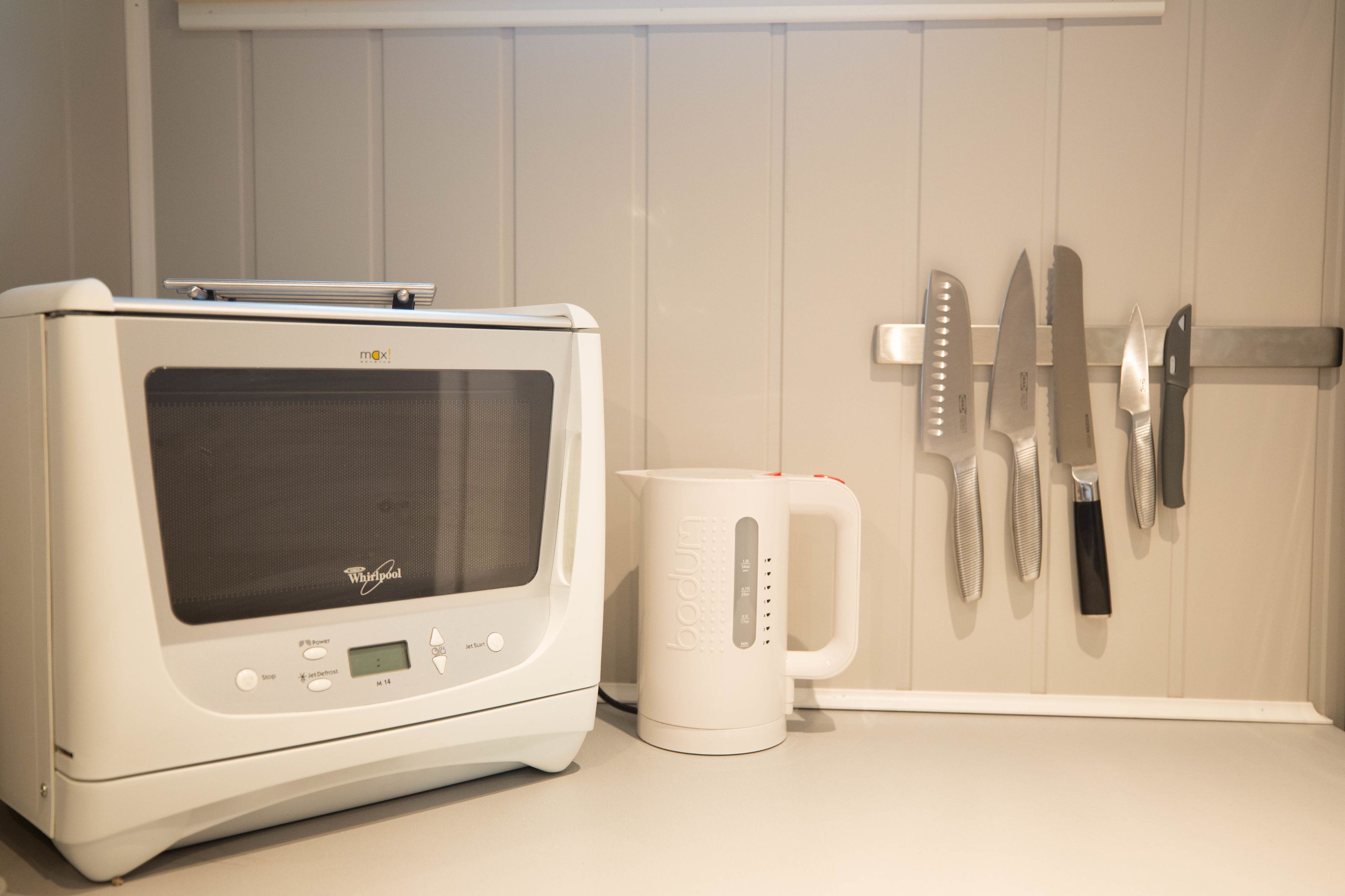 Una cocina con microondas, cafetera y cuchillos colgados en la pared.