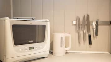 Una cocina con microondas, cafetera y cuchillos colgados en la pared.