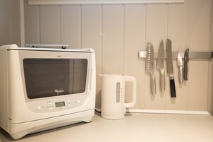 Una cocina con microondas, cafetera y cuchillos colgados en la pared.