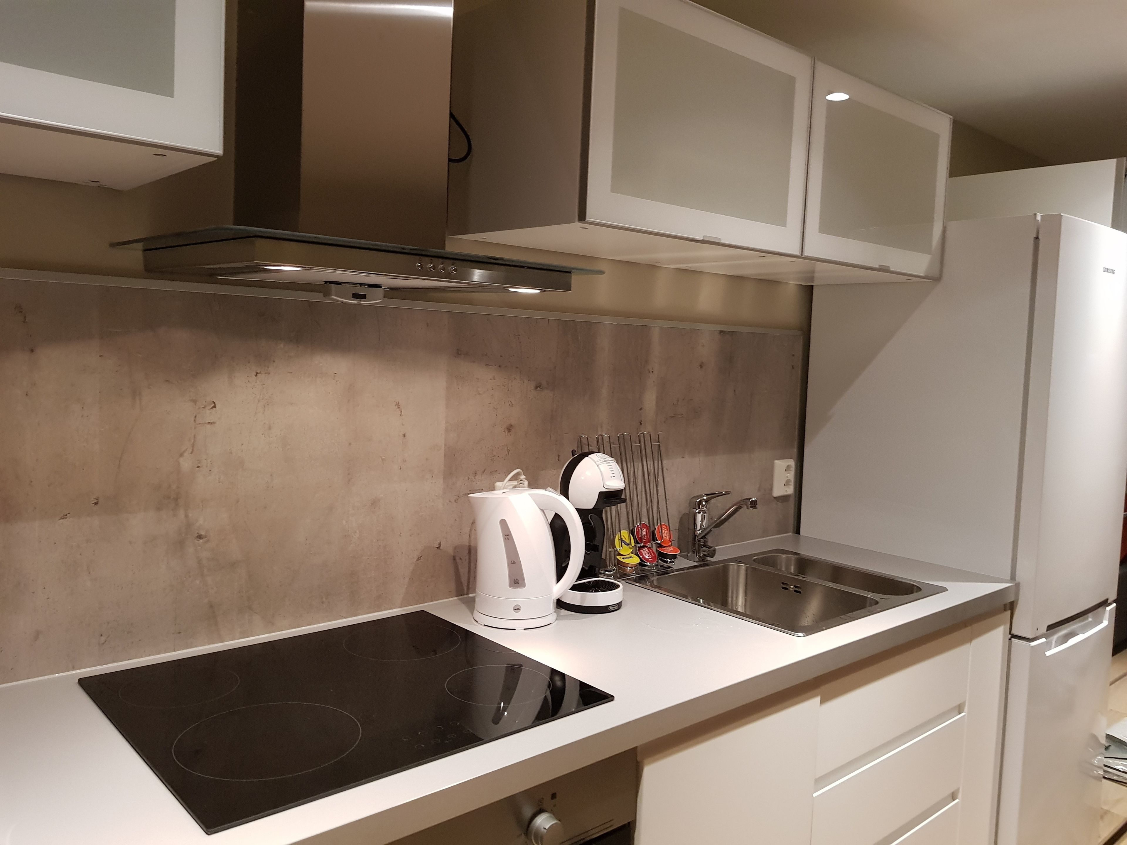 Une cuisine moderne avec des meubles blancs, une hotte en acier inoxydable, une plaque de cuisson à induction, une machine à café et un évier.