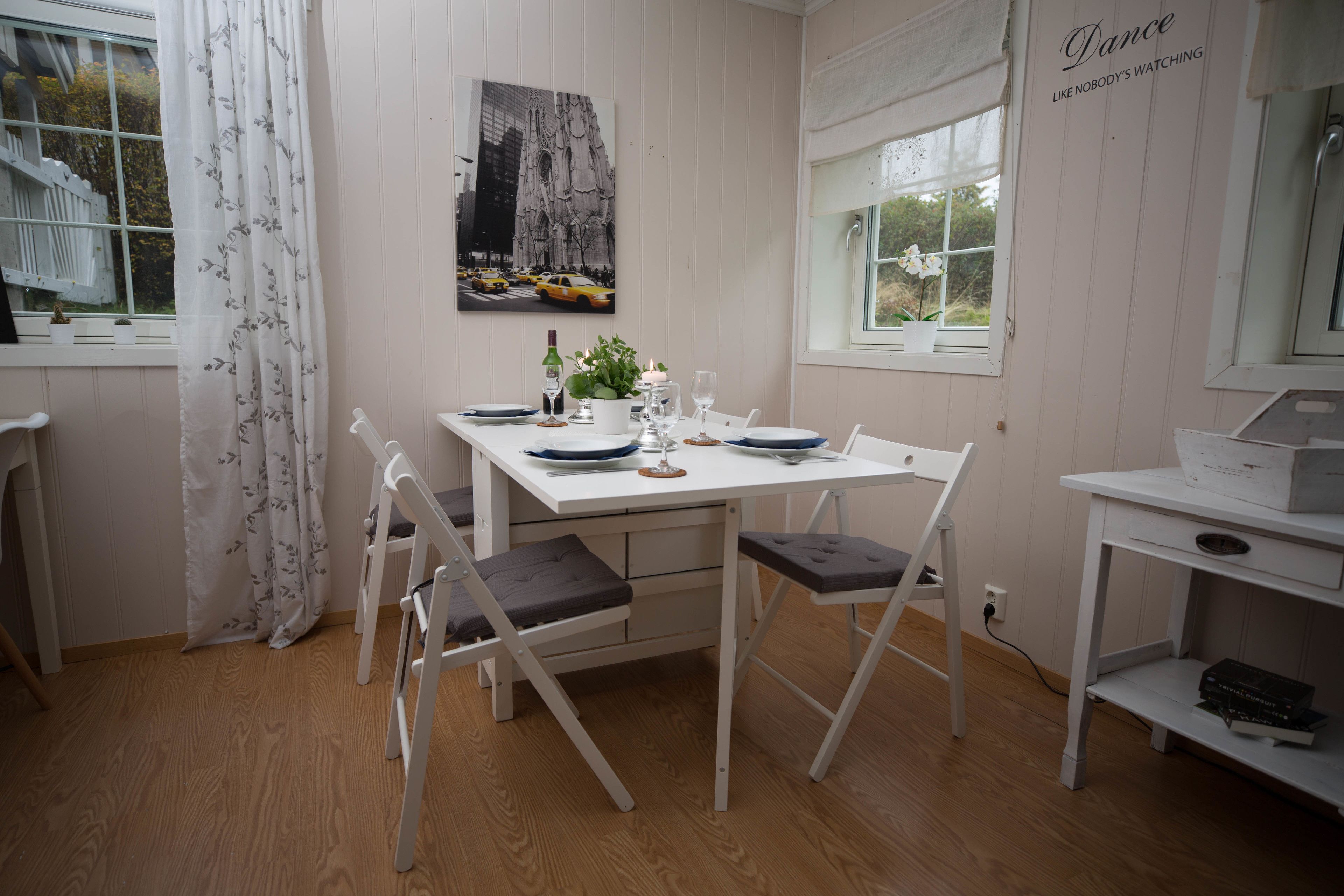 Et spiseområde med et hvidt bord, stole og et vindue med udsigt til en bygning.