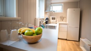 A kitchen with a wooden bowl of green apples and bananas on the counter, a white refrigerator, and a window providing natural light.