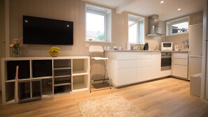A modern kitchen with white cabinetry, a flat-screen TV mounted on the wall, a microwave, and a refrigerator.