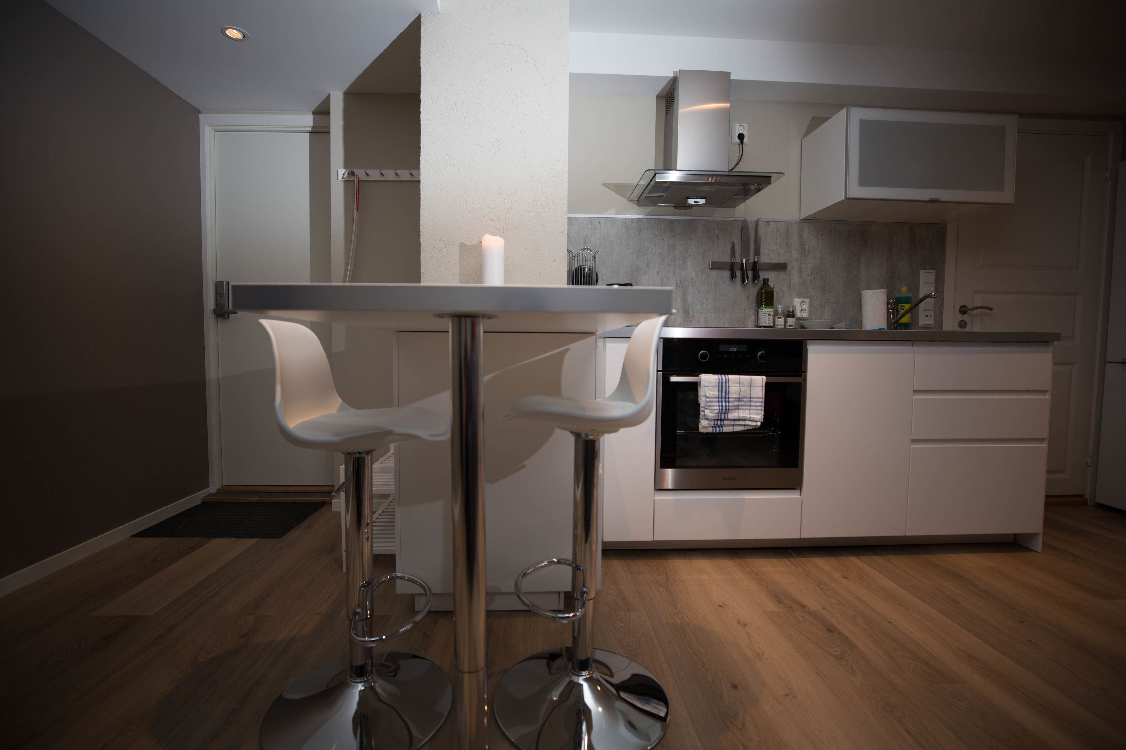 A modern kitchen with two bar stools, a built-in oven, and a stainless steel range hood.