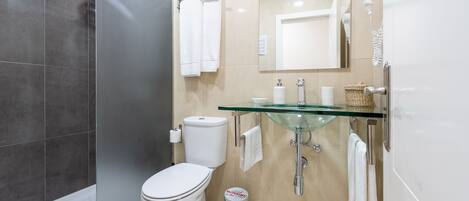 Une salle de bain moderne avec un lavabo en verre, des toilettes, une douche et un porte-serviettes.
