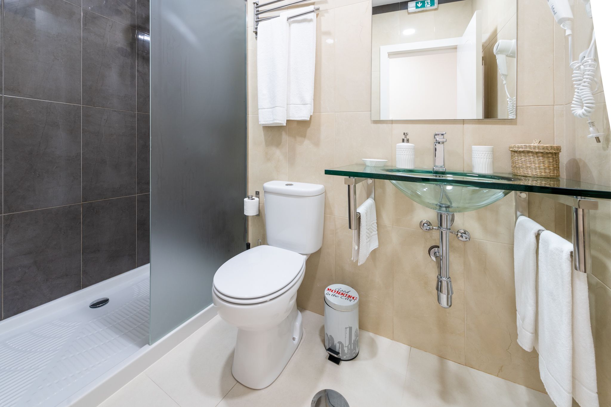 A modern bathroom with a glass sink, a toilet, and a shower area.