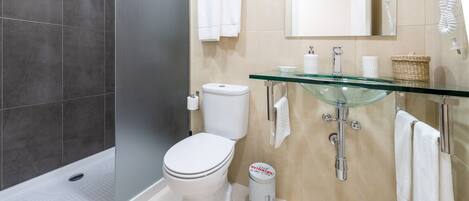 A modern bathroom with a glass sink, a toilet, and a shower area.