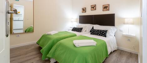 A hotel room with two beds, green bedspreads, a large mirror, a chandelier, and wall-mounted artwork.