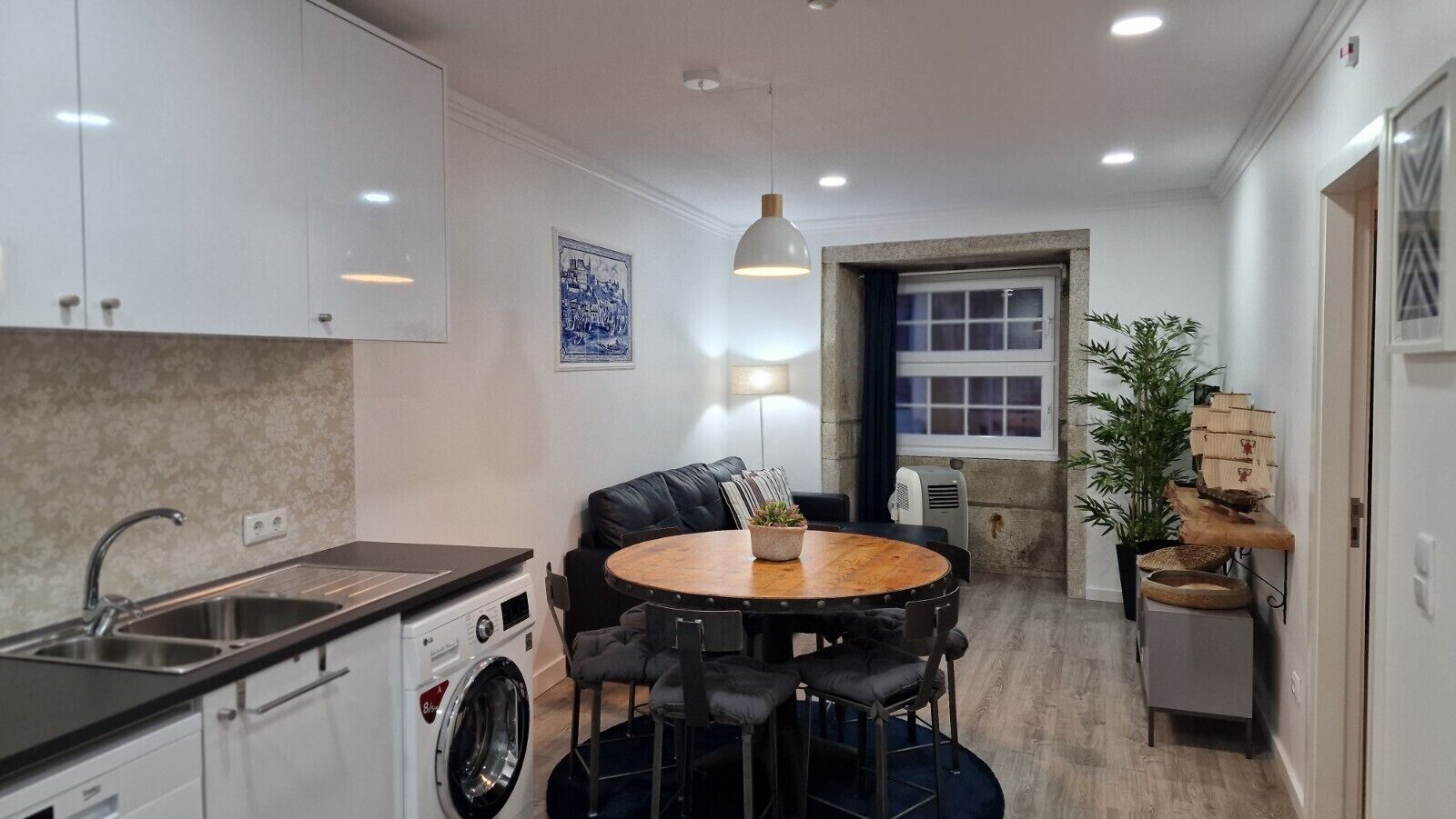 A compact kitchen with a sink, washing machine, and a dining area with a round table and chairs.