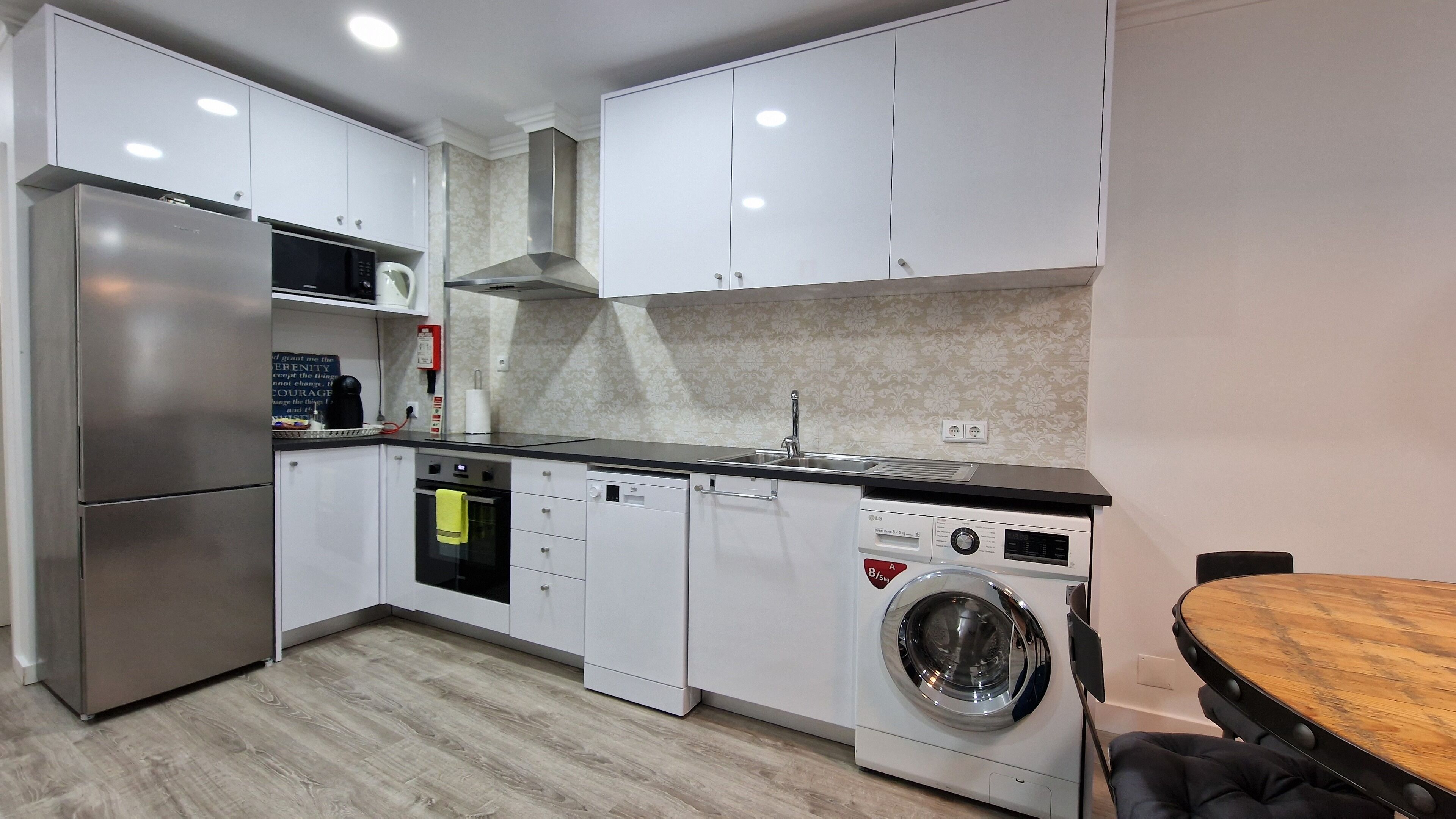 A modern kitchen with white cabinets, a stainless steel refrigerator, a built-in oven, a dishwasher, and a washing machine.