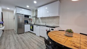 A modern kitchen with white cabinets, stainless steel appliances, and a wooden dining table with a potted plant. - Merc Porto Ribeira View (Porto)