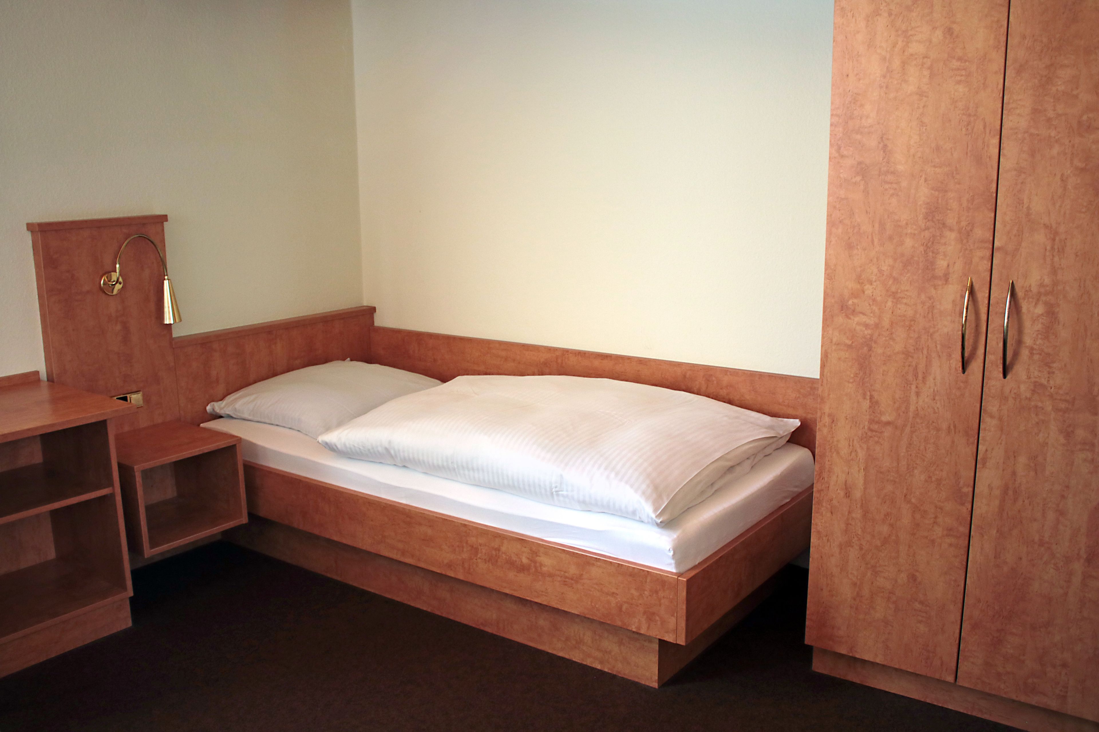Una cama individual con cabecera y piecera de madera, una mesita de noche y un armario de dos puertas.