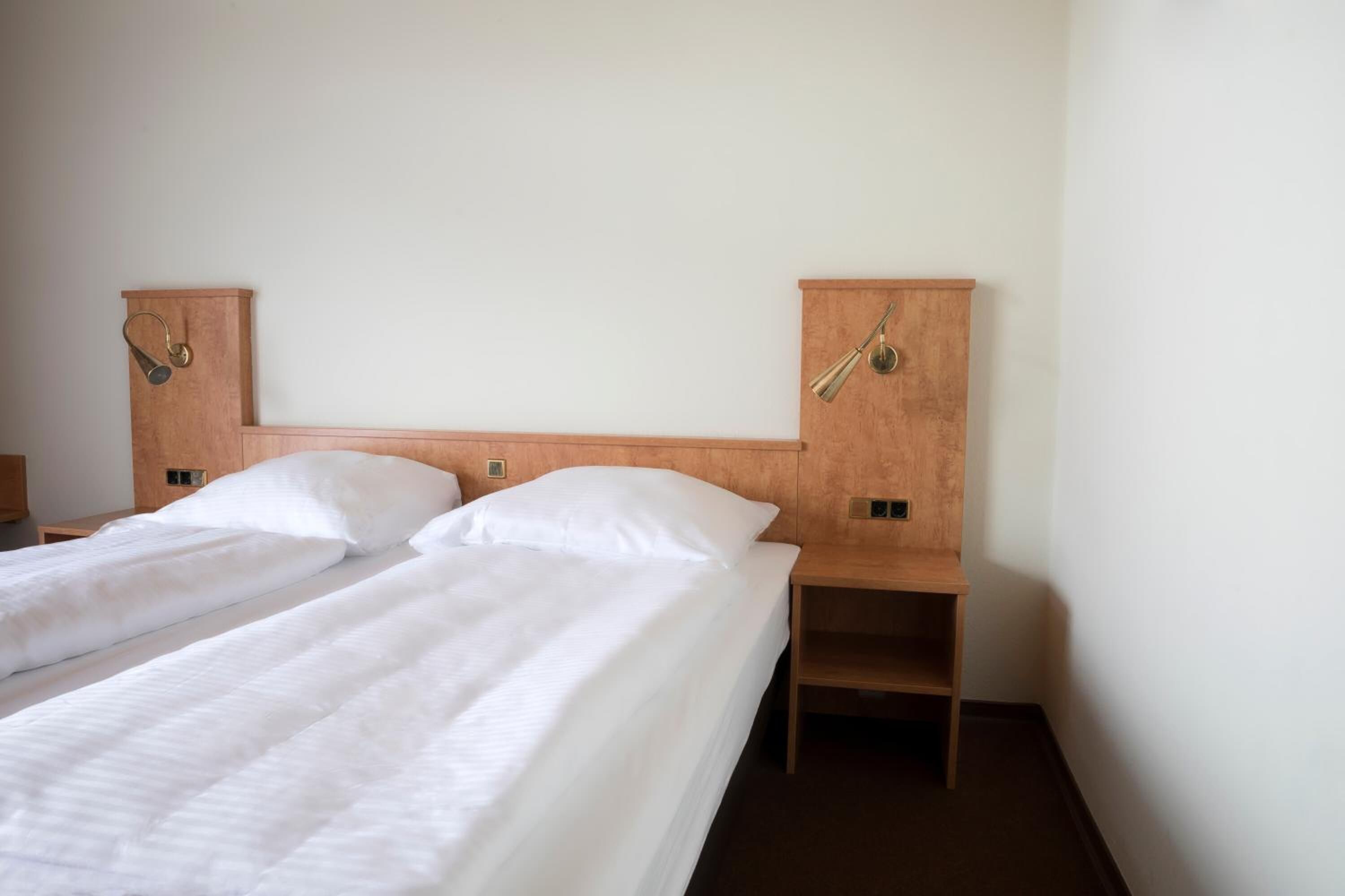 Ein Hotelzimmer mit zwei Einzelbetten, Holz-Kopfteilen und Nachttischen.
