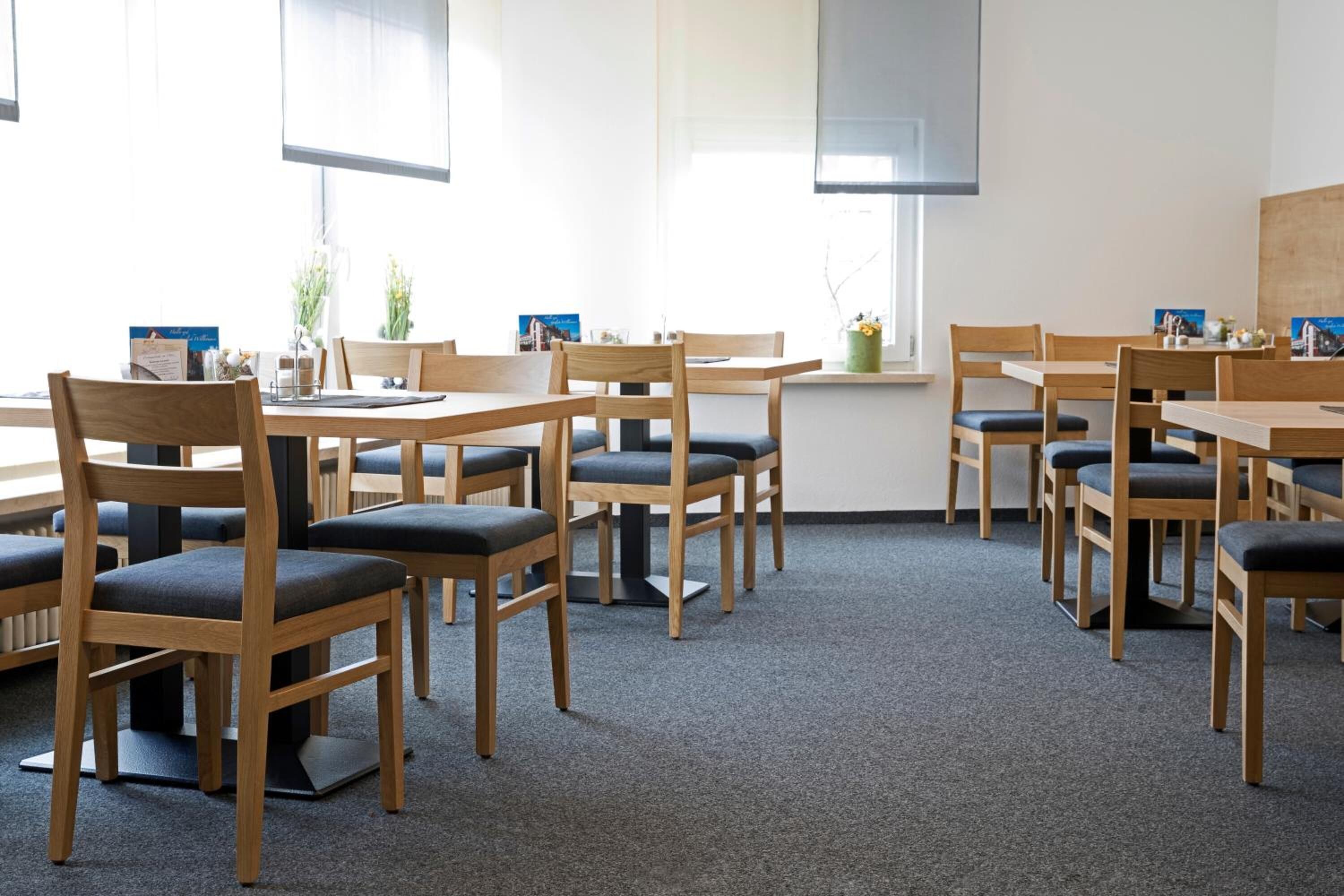 A conference room with wooden tables and chairs, carpeted floor, and large windows.