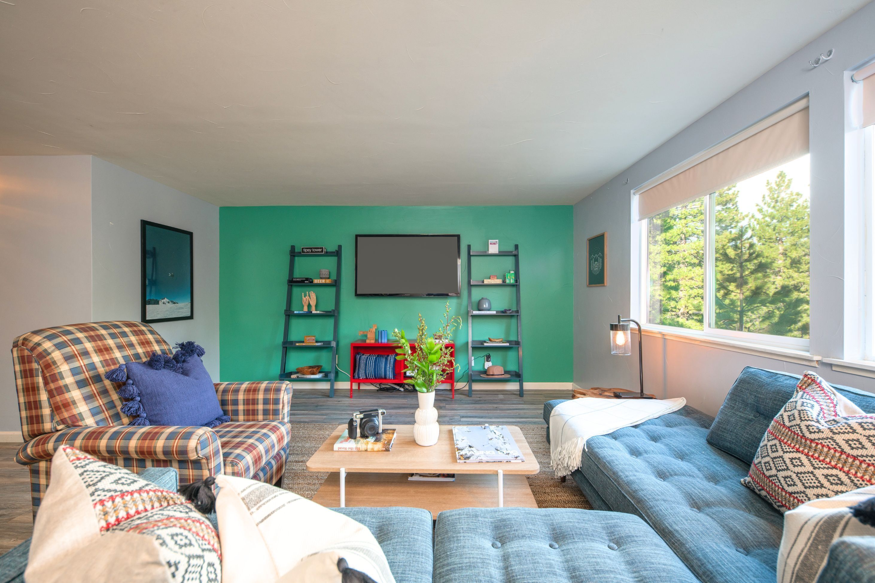 Un salon avec un mur d’accent de couleur turquoise, un fauteuil à carreaux, un canapé bleu et une table basse agrémentée d’un vase et de livres.