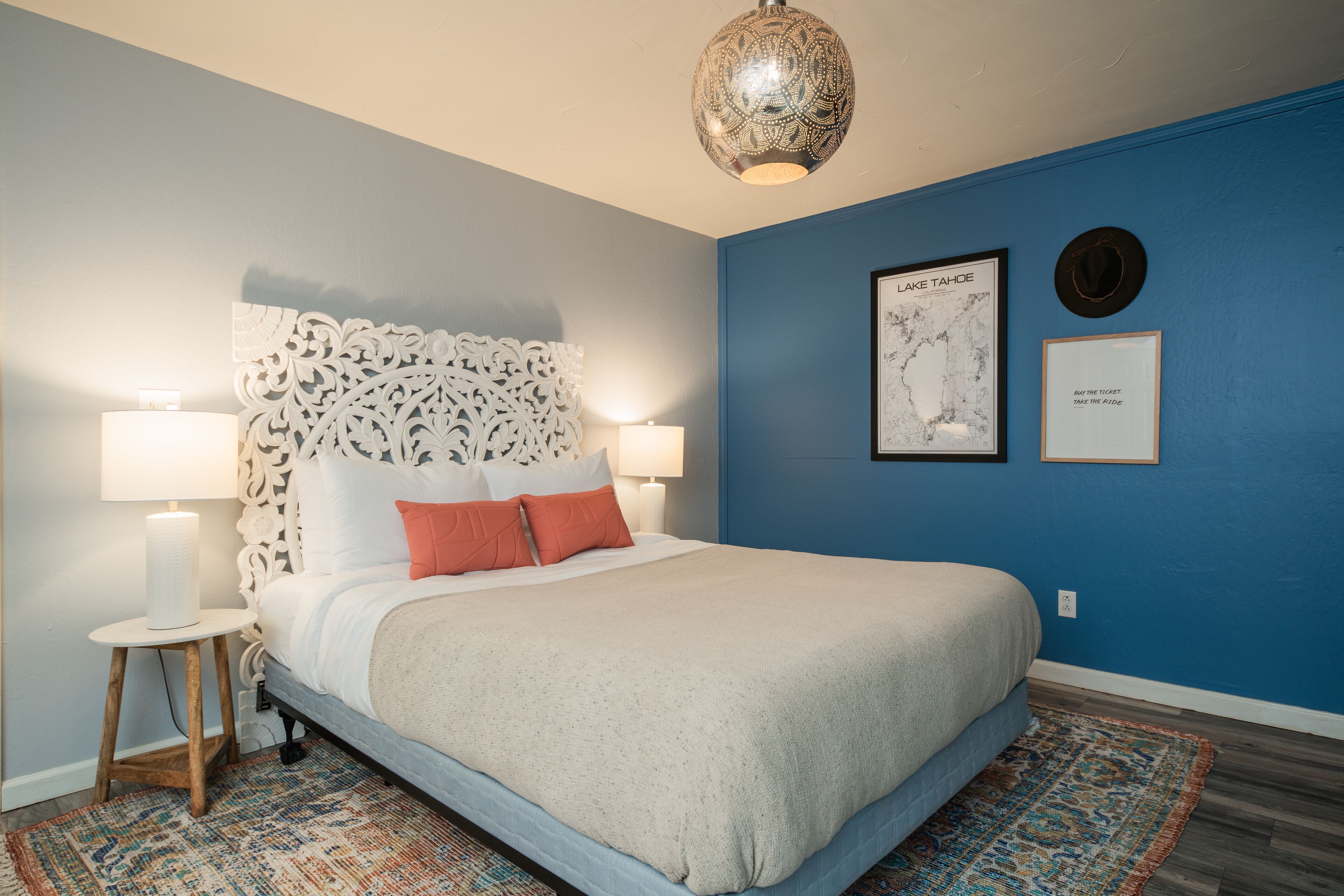 A bedroom with a bed, two bedside lamps, a decorative headboard, a map, and a framed quote on the wall.