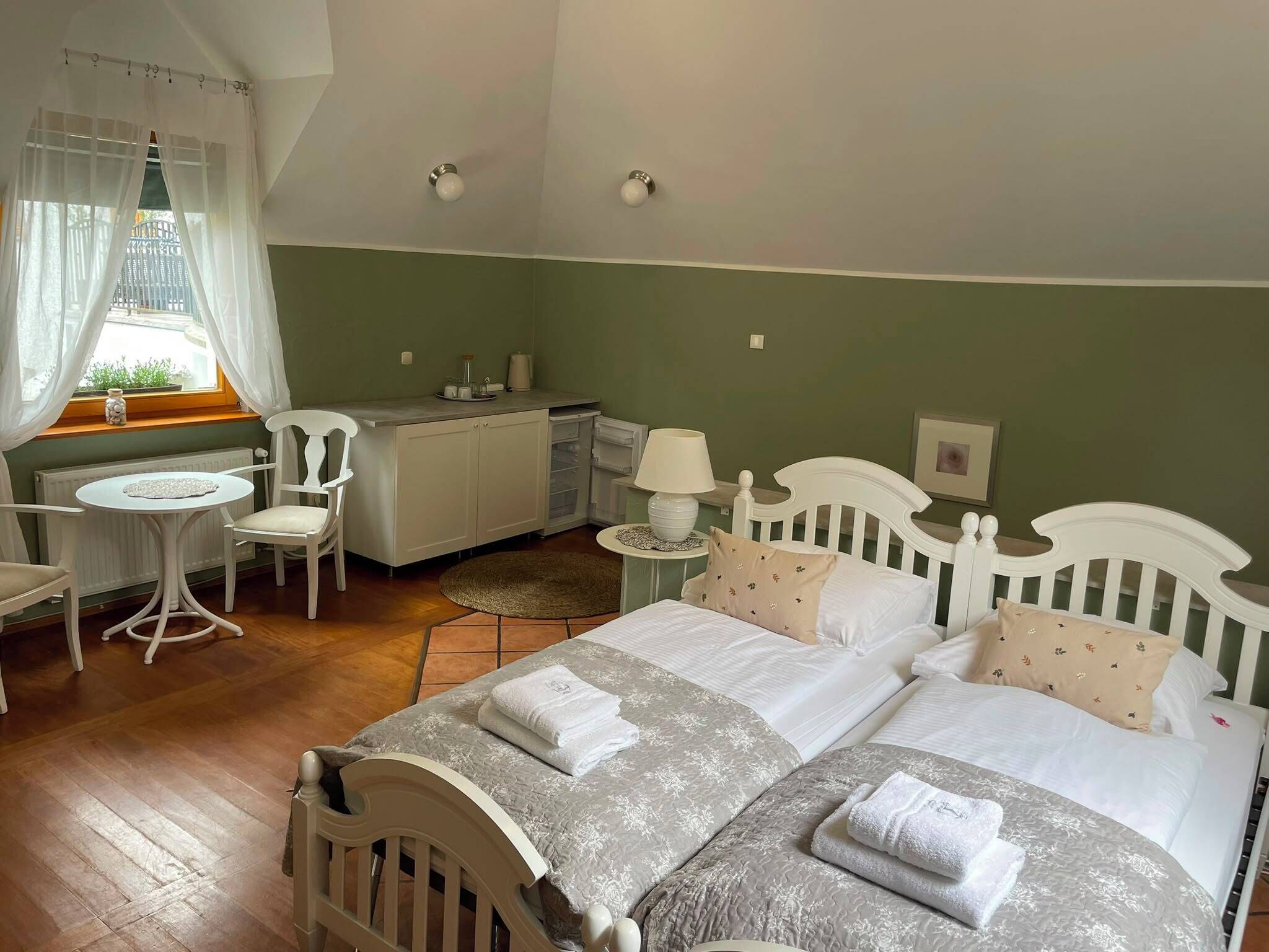 A bedroom with a bed, bedside tables, a chair, a small round table, and a window with curtains.