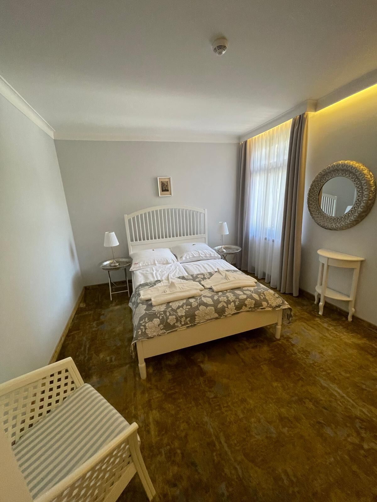 A bedroom with a bed, bedside tables, a mirror, and a window with curtains.