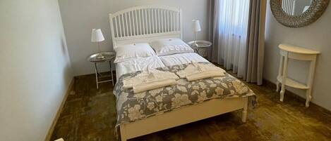 A bedroom with a bed, bedside tables, a mirror, and a window with curtains.