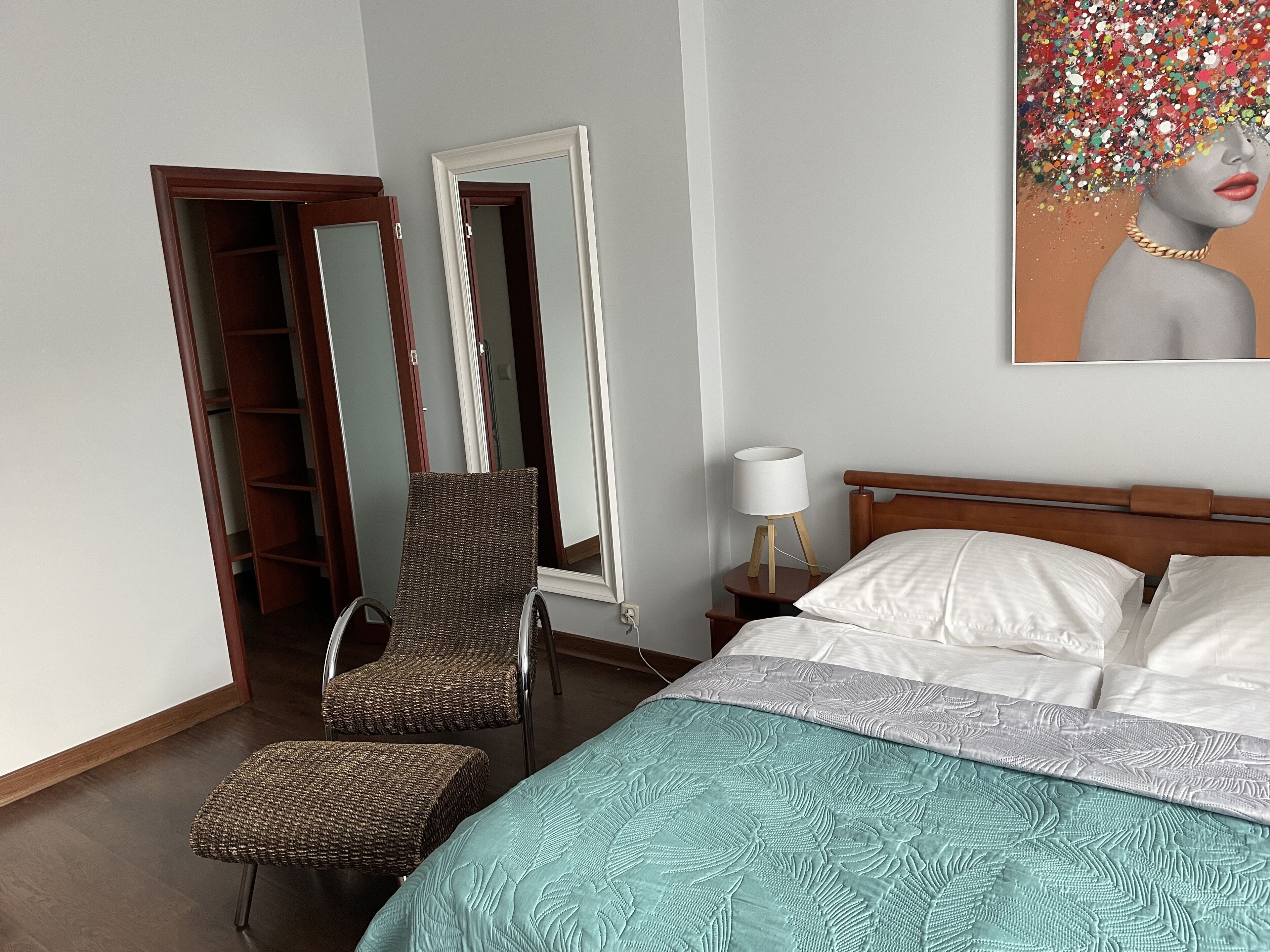 A bedroom with a bed, a chair, a nightstand, and a mirror.
