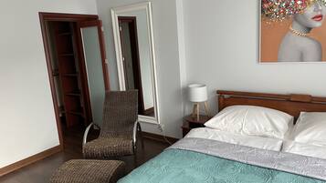 A bedroom with a bed, a chair, a nightstand, and a mirror.